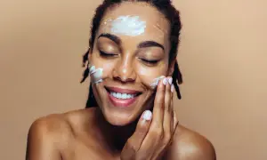 Une femme applique une crème hydratante sur son visage, un geste essentiel pour un maquillage jour parfait.