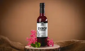 Butelka syropu z derenia, ozdobiona gałązkami różowych kwiatów i miętą. Idealny do domowych deserów, jak w przepisie na syrop z derenia.