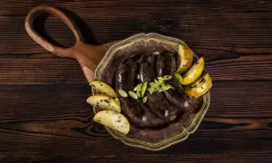 Pyszna kaszanka z piekarnika, podana z pieczonymi ziemniakami i szczypiorkiem, na drewnianej desce.