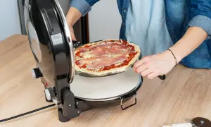Osoba wkłada surową pizzę z szynką do czarnego pieca do pizzy.