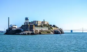 Słynne więzienie Alcatraz na skalistej wyspie, z charakterystyczną wieżą ciśnień i mostem w tle.