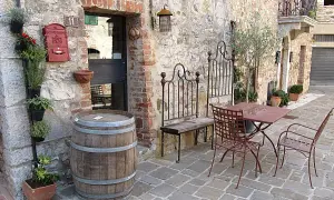 Un angolo pittoresco nella regione del Chianti con un barile di legno, piante aromatiche, un tavolino da esterno e un vecchio cancello in ferro battuto.