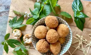 Goldbraune Arancini, frisch zubereitet nach einem tollen arancini rezept, liegen in einer Schale. Frische Kräuter und Holzspieße zieren die Holzplatte.