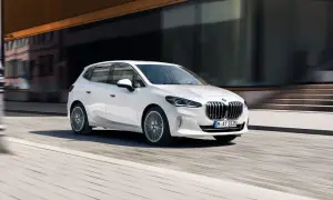 Biały BMW 2 Active Tourer w ruchu miejskim, z rozmytym tłem budynków i ulicy.