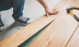 Pose d'un parquet flottant, une main ajuste une lame. Outil et maillet à proximité.