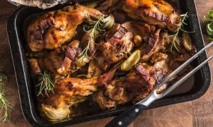 Coniglio panato al forno, dorato e succulento, con pancetta croccante, cipolle e rosmarino in una teglia.