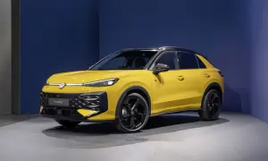 Żółty Volkswagen T-Roc VW z czarnym dachem i felgami stoi na szarej podłodze przed niebieską ścianą.