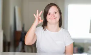 Ragazza con sindrome di down sorride e fa il segno "ok" con la mano.