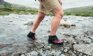 Nogi w krótkich spodenkach i trekkingowych butach przechodzą przez strumień. Idealna pogoda, by sprawdzić, od ilu stopni krótkie spodenki są komfortowe.