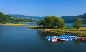 Jezioro Żywieckie, z kolorowymi rowerami wodnymi przy brzegu, otoczone zielonymi wzgórzami. Głębokość jeziora zachęca do wodnych zabaw.