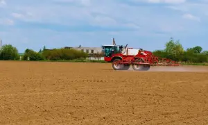 Czerwony opryskiwacz rolniczy, prawdopodobnie z preparatem chlomazon, przejeżdża przez zaorane pole, przygotowując je do siewu.