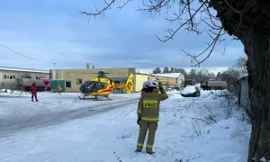 Śnieg, śmigłowiec ratunkowy i strażak na tle budynków. Sytuacja wygląda na izolowane zdarzenie medyczne.