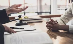 Prawnik omawia z klientem formalności związane z postępowaniem spadkowym. Na stole leży młotek sędziowski i dokumenty.