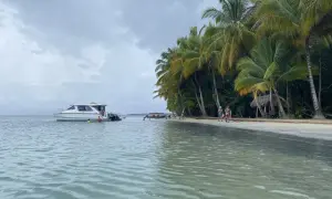 Rajska plaża na San Blas z palmami, łodzią i ludźmi kąpiącymi się w turkusowej wodzie.