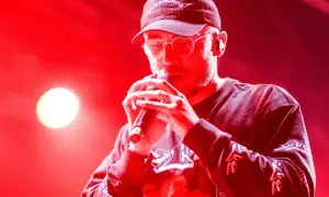 Raper w czapce i okularach śpiewa do mikrofonu. Jego album zdobył Fryderyka w kategorii album roku (hip-hop).