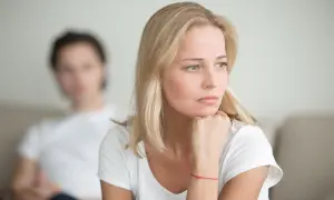 Zamyślona kobieta z czerwoną nitką na nadgarstku, zastanawia się, kto powinien odezwać się po rozstaniu. W tle niewyraźna postać mężczyzny.