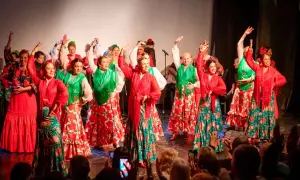 Un grupo de mujeres baila sevillanas de amor con trajes coloridos. Sus faldas amplias y mantones vibrantes llenan el escenario de alegría.