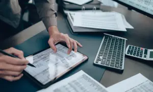 Osoba pracująca na tablecie z arkuszem kalkulacyjnym, obok klawiatura i kalkulator.