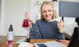 Uśmiechnięta influencerka z pomadką na dłoni pokazuje, jak zostać ambasadorem marki, nagrywając tutorial makijażowy.