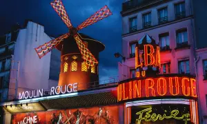 Le Moulin Rouge à Paris s'illumine la nuit, ses ailes de moulin rouge et jaune dansant sous le ciel sombre.