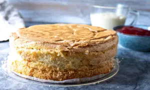 En gyllene tårtbotten, redo för ett tårtbotten recept. Bredvid står en skål med sylt och en kanna med grädde.
