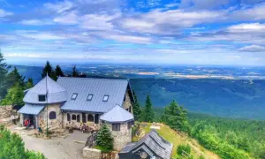 Kamienny schron turystyczny na szlaku w Górach Izerskich. Rozległa panorama krajobrazu z lasami i polami w oddali.