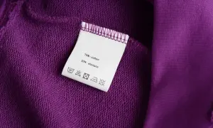 Metka na fioletowej tkaninie: 70% bawełna, 30% elastan. Miękki materiał, idealny na wygodne ubrania.