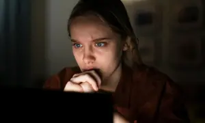 Przerażona dziewczyna wpatruje się w ekran, czując się jak ofiara stalkingu.