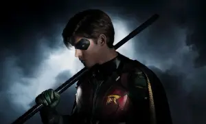 Robin z obsady Titans, z maską na oczach i kostiumem z symbolem R, trzyma pałkę.