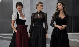 Drei Frauen in eleganten Dirndln. Das schwarze Dirndl mit Spitzenärmeln und dezentem Muster steht für moderne Eleganz.
