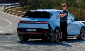 Młody mężczyzna w okularach stoi obok sportowego Hyundai Ioniq 5 N na krętej drodze.