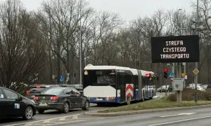 Autobus i samochody stoją w korku pod znakiem informującym o krakowskiej strefie czystego transportu.