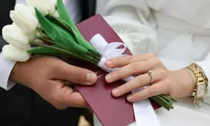 Dłoń mężczyzny i kobiety trzymają bukiet białych tulipanów i czerwony dokument.