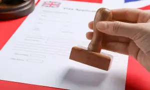 Dłoń trzyma pieczątkę nad formularzem wniosku o wizę do Anglii.