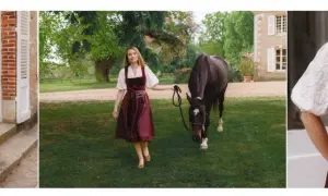 Eine Frau in einem weinroten Dirndl mit einer glänzenden Dirndlschürze aus Seide, daneben ein Pferd auf einer grünen Wiese.