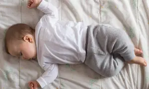 Un neonato non dorme, ma riposa sul fianco, vestito di bianco e grigio, su un lenzuolo con fiori stilizzati.