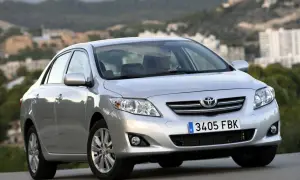 Srebrna Toyota Corolla 2010 z widocznym kierowcą, zaparkowana na tle krajobrazu z budynkami.