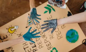 Manos pintadas de azul y gris sobre un cartel con dibujos de la Tierra, una bombilla y el símbolo de reciclaje. Un llamado a la acción para salvar el planeta.