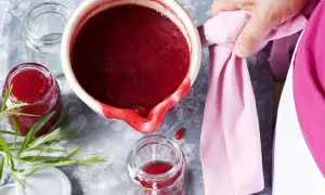 Frisch gekochte, einfache Johannisbeermarmelade wird in ein Glas gefüllt. Ein Hauch von Grün und ein rosa Tuch vervollständigen das Bild.