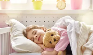 Mała dziewczynka śpi spokojnie z misiem, co jest przeciwieństwem problemów z zaburzeniami snu u dzieci.