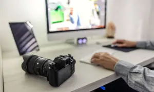Aparat fotograficzny leży obok tabletu, a osoba przy komputerze pracuje nad zdjęciami. To pokazuje, jak zgrać zdjęcia z aparatu na laptop.