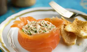 Ein appetitlicher **Salat mit Fisch**, serviert in einem Lachs-Cup, mit knusprigen Brotscheiben und einer goldenen Gabel.