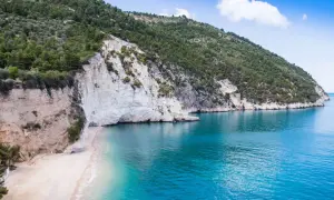 Spiaggia di Vignanotica, con scogliere bianche a picco sul mare turchese e una collina verdeggiante.
