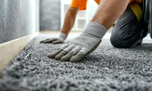 Rękawiczki pomagają przykleić wykładzinę dywanową do ściany. Pracownik dociska szarą wykładzinę.