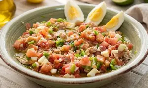 Un refrescante plato de pipirrana andaluza, con tomate, pimiento, huevo duro y atún, listo para disfrutar.