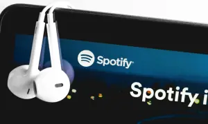 Białe słuchawki wiszą na ekranie smartfona z logo Spotify.