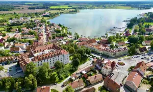 Malowniczy widok na miasteczko nad jeziorem w regionie Warmia i Mazury. Zamek, kolorowe kamienice i przystań jachtowa tworzą urokliwy krajobraz.