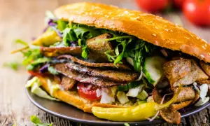Apetyczny kebab w bułce z mięsem, warzywami i sosem na drewnianym tle.