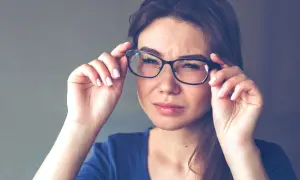 Kobieta z niedowidzeniem na jedno oko poprawia okulary, marszcząc czoło.