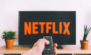 En hand håller en fjärrkontroll framför en TV med Netflix-loggan. Perfekt för bra filmtips ikväll!